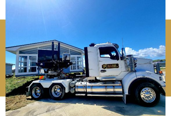 A weatherboard house lifted clear of its foundations on a hydraulic house trailer, ready to move